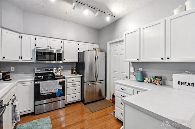 kitchen with appliances with stainless steel finishes, light countertops, white cabinetry, and light wood-style floors