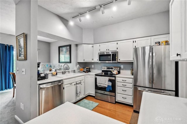 kitchen with stainless steel appliances, a sink, track lighting, white cabinetry, and light countertops
