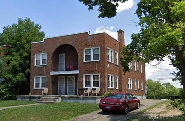 view of front of house with a chimney, a balcony, brick siding, a front yard, and asphalt driveway