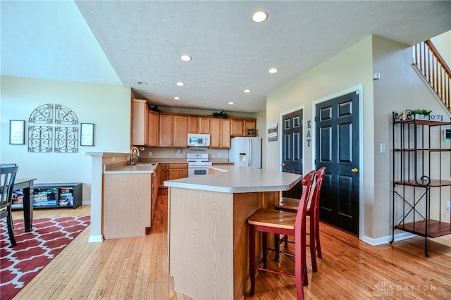 kitchen featuring white appliances, light wood finished floors, light countertops, a sink, and recessed lighting