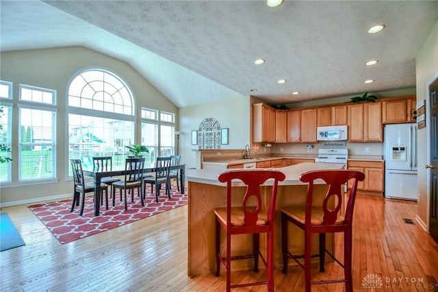 kitchen featuring white appliances, a sink, light countertops, lofted ceiling, and light wood-style floors