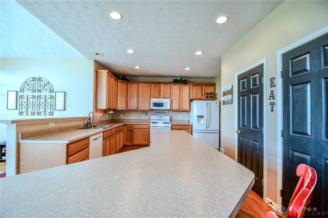 kitchen with white appliances, a sink, a peninsula, recessed lighting, and light countertops