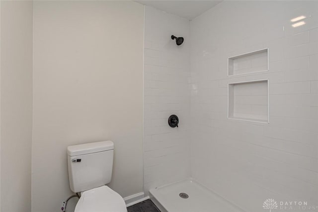 full bath with tiled shower, toilet, and baseboards