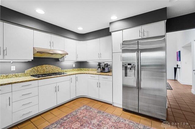 1900 Kresswood Cir, Kettering, OH 45429 - kitchen featuring stainless steel refrigerator with ice dispenser, under cabinet range hood, light tile patterned flooring, white cabinets, and gas cooktop
