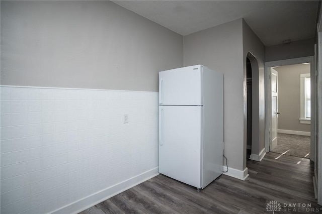 kitchen featuring freestanding refrigerator, dark wood-style flooring, baseboards, and arched walkways