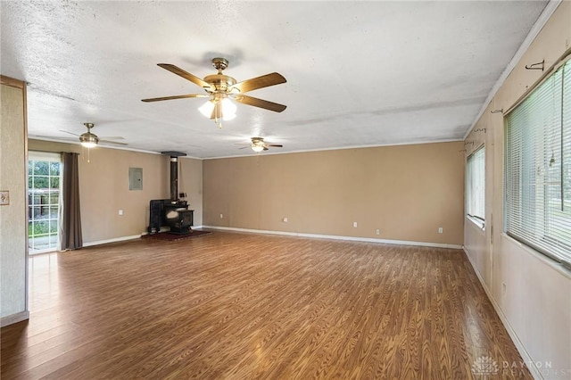 unfurnished living room featuring wood finished floors, a wood stove, ceiling fan, baseboards, and ornamental molding