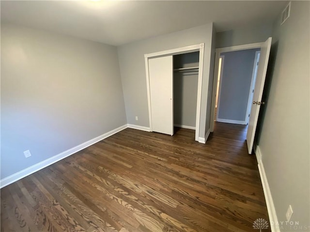 unfurnished bedroom featuring baseboards, dark wood-style floors, and a closet