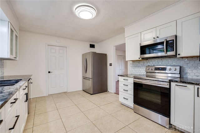 kitchen with appliances with stainless steel finishes, tasteful backsplash, dark stone counters, and white cabinets