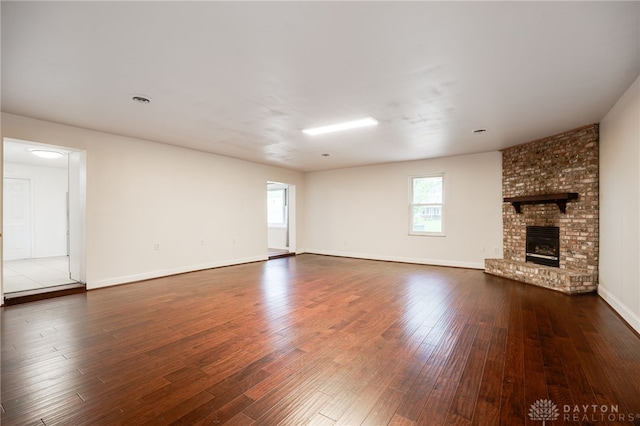 unfurnished living room featuring dark wood finished floors, a brick fireplace, and baseboards