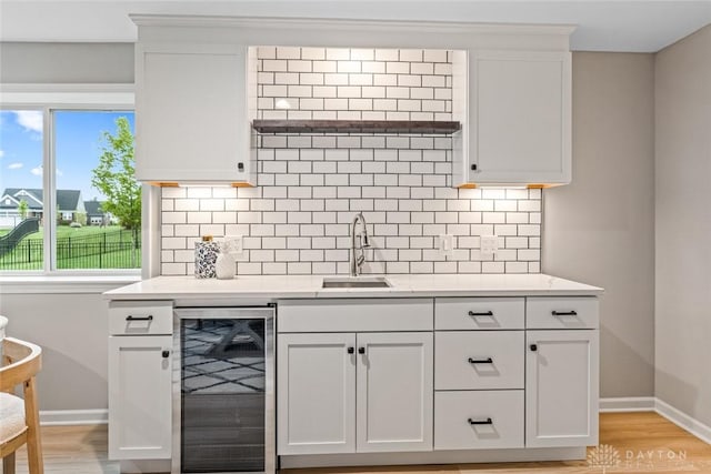kitchen featuring wine cooler, a sink, baseboards, and decorative backsplash