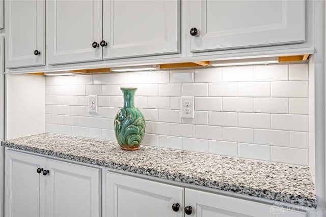 detailed view of tasteful backsplash, white cabinets, and light stone countertops