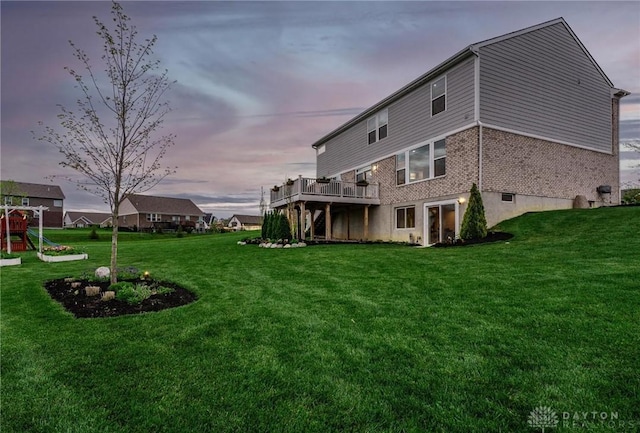 back of property with a yard, a deck, and brick siding