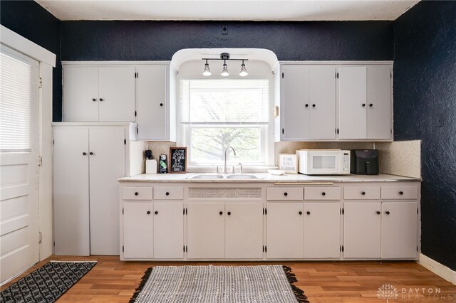 1000 Haviland Ave, Dayton, OH 45410 - kitchen with a sink, white microwave, light wood finished floors, a textured wall, and white cabinets