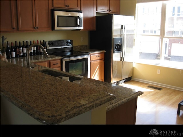 4324 Straight Arrow Rd, Beavercreek, OH 45430 - kitchen featuring appliances with stainless steel finishes, light wood-style floors, dark stone countertops, and brown cabinetry