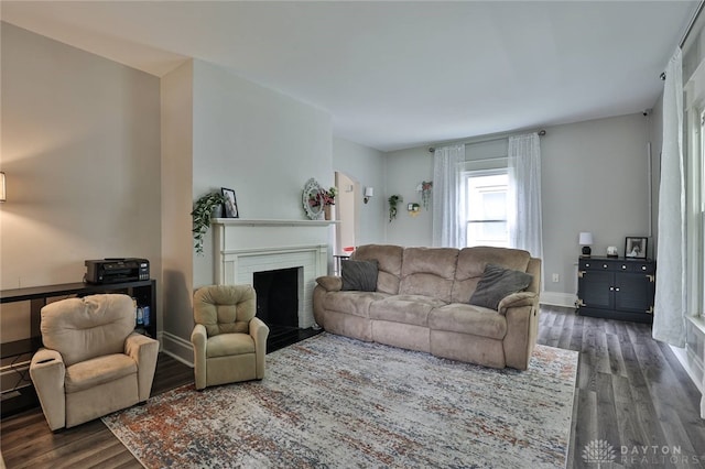 living area featuring dark wood-style flooring, a brick fireplace, and baseboards