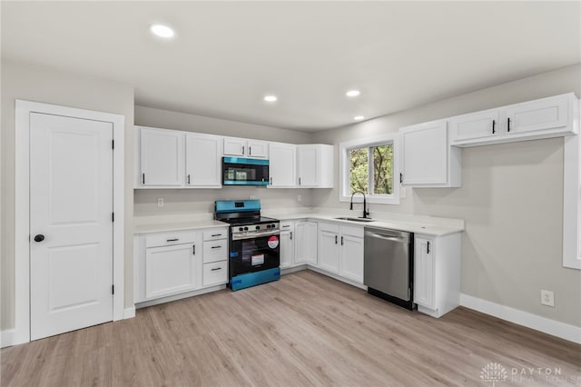 kitchen featuring appliances with stainless steel finishes, a sink, white cabinetry, light wood-style floors, and baseboards