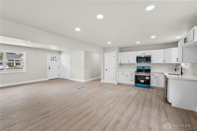 kitchen with stainless steel appliances, a sink, light wood finished floors, light countertops, and recessed lighting