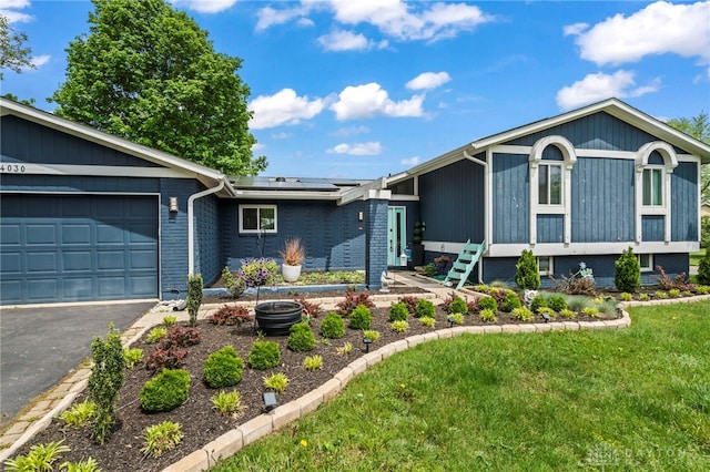 view of front facade with roof mounted solar panels, an attached garage, a front yard, asphalt driveway, and brick siding