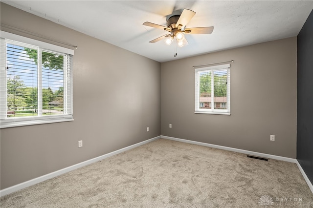 empty room with plenty of natural light, ceiling fan, and carpet flooring