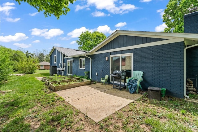 back of property featuring a garden, brick siding, a patio, a lawn, and cooling unit