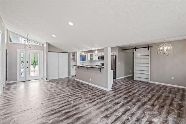 unfurnished living room featuring a barn door, dark wood-style flooring, a textured ceiling, recessed lighting, and vaulted ceiling