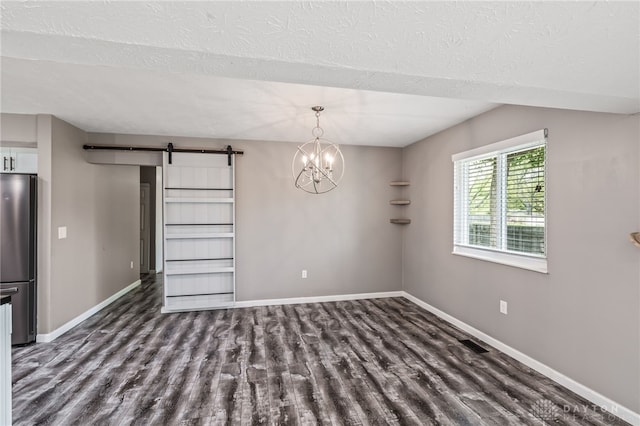 unfurnished dining area featuring wood finished floors, a barn door, baseboards, and a textured ceiling