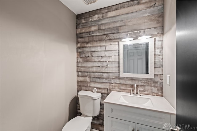 half bath with toilet, vanity, and wooden walls