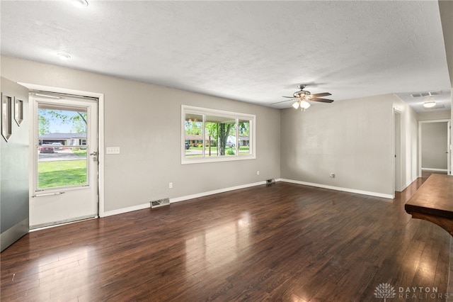 unfurnished living room with plenty of natural light, dark wood finished floors, a textured ceiling, a ceiling fan, and baseboards