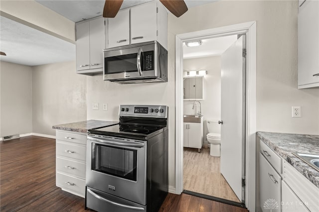kitchen featuring appliances with stainless steel finishes, ceiling fan, dark wood finished floors, white cabinetry, and baseboards