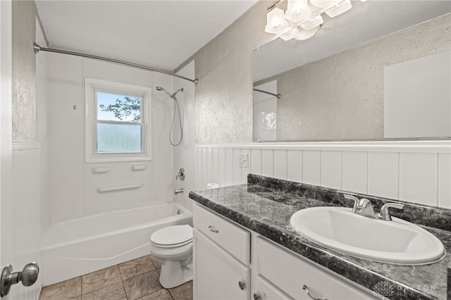 full bath with a textured wall, bathtub / shower combination, toilet, vanity, and a wainscoted wall