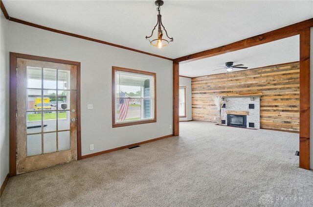 unfurnished living room featuring wood walls, healthy amount of natural light, carpet flooring, crown molding, and baseboards