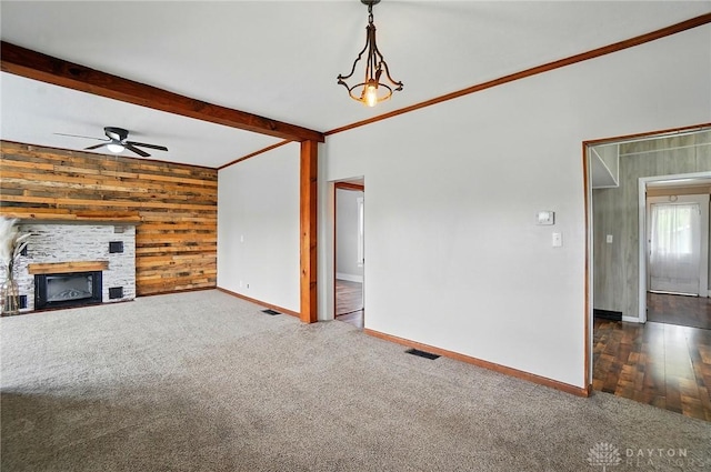 unfurnished living room featuring carpet flooring, ceiling fan, baseboards, wooden walls, and a fireplace