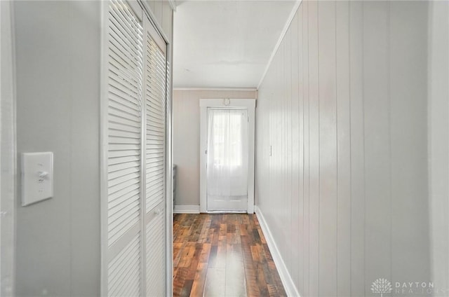 hallway featuring dark wood-style flooring, crown molding, baseboards, and wooden walls