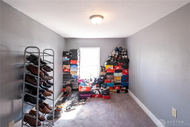 recreation room with carpet flooring, a textured ceiling, a textured wall, and baseboards