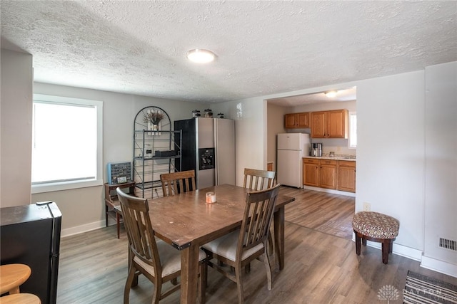 dining room with light wood-style flooring, a textured ceiling, and baseboards