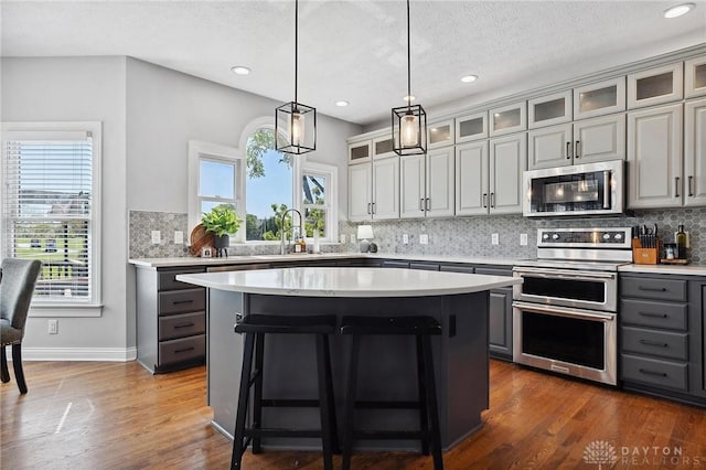 kitchen with appliances with stainless steel finishes, gray cabinets, light countertops, tasteful backsplash, and recessed lighting