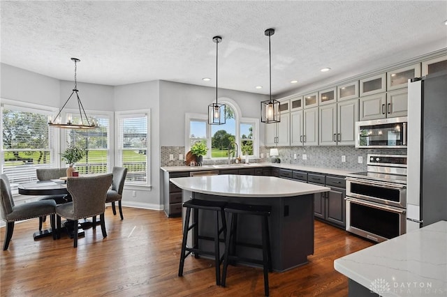 kitchen with appliances with stainless steel finishes, a textured ceiling, a center island, tasteful backsplash, and recessed lighting