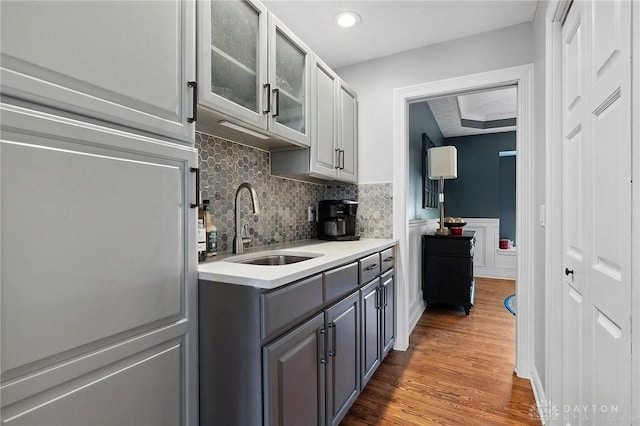 kitchen with gray cabinetry, a sink, light countertops, glass insert cabinets, and wood finished floors