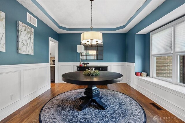 dining area with a tray ceiling, a chandelier, plenty of natural light, dark wood-style floors, and a wainscoted wall