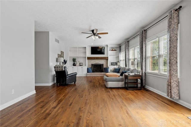 living room with a ceiling fan, baseboards, a brick fireplace, a textured ceiling, and wood finished floors