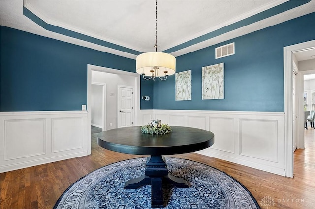 dining room with wood finished floors, a wainscoted wall, a raised ceiling, ornamental molding, and a decorative wall