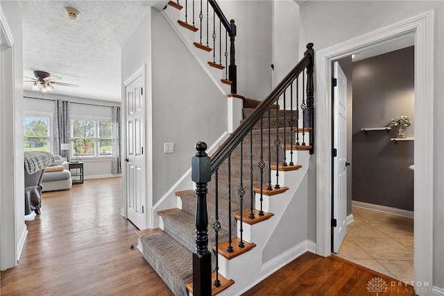 stairs featuring wood finished floors, ceiling fan, baseboards, and a textured ceiling