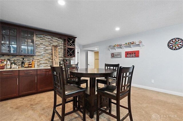 dining area featuring light colored carpet, bar with sink, recessed lighting, baseboards, and a textured ceiling