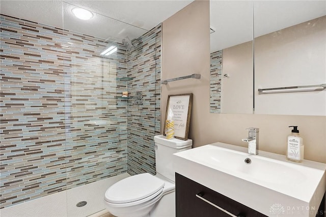 full bathroom featuring toilet, a tile shower, and vanity