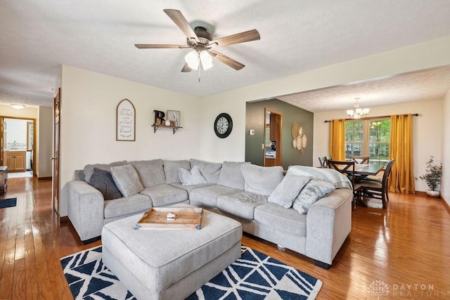 living room featuring a chandelier, light wood-style flooring, a ceiling fan, and a textured ceiling