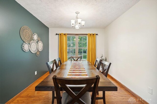 dining area featuring a chandelier, a textured ceiling, light wood-style floors, and baseboards