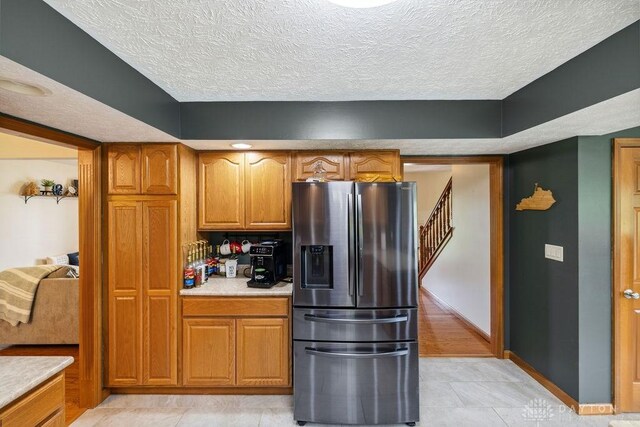 kitchen with stainless steel refrigerator with ice dispenser, light countertops, brown cabinetry, a textured ceiling, and light tile patterned flooring