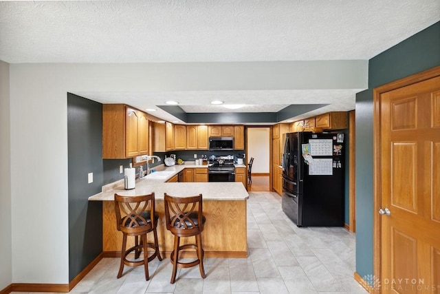 kitchen with black appliances, a sink, a peninsula, light countertops, and baseboards