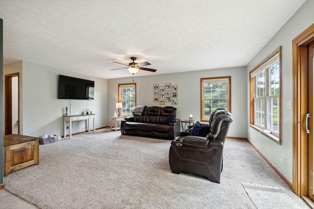 living area with healthy amount of natural light, light carpet, a ceiling fan, a textured ceiling, and baseboards