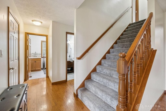 entrance foyer featuring light wood-style flooring, stairway, baseboards, and a textured ceiling